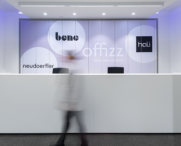 Weiße Empfangstheke vor Markenwand mit hali, Bene und Neudoerfler Logos.