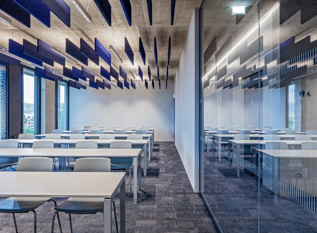 Schulungsraum mit weißen Möbeln und schwebenden Akustikelementen in Blau