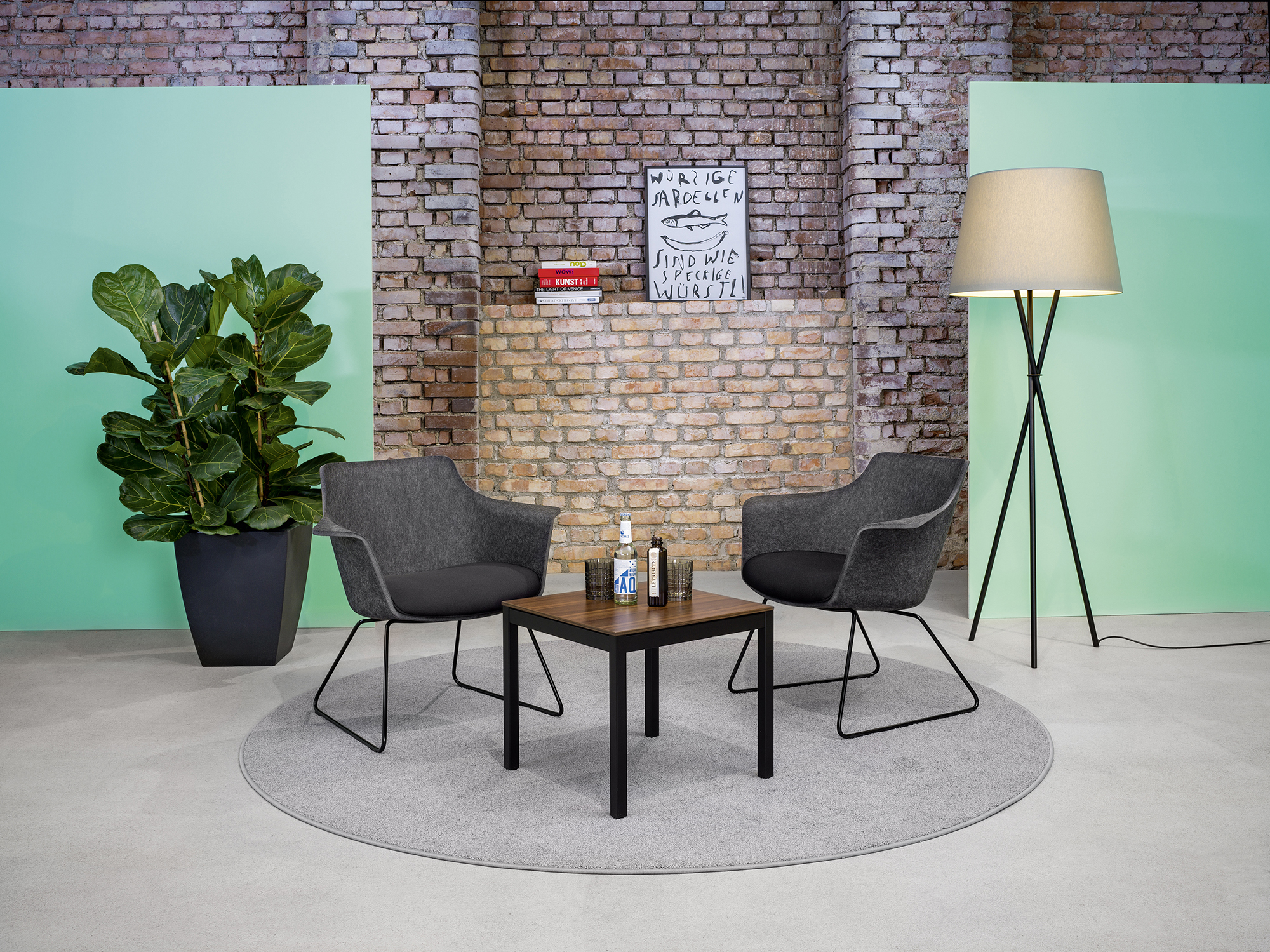 Zwei graue Lounge-Stühle mit Couchtisch auf rundem Teppich in gemütlicher Meeting-Ecke
