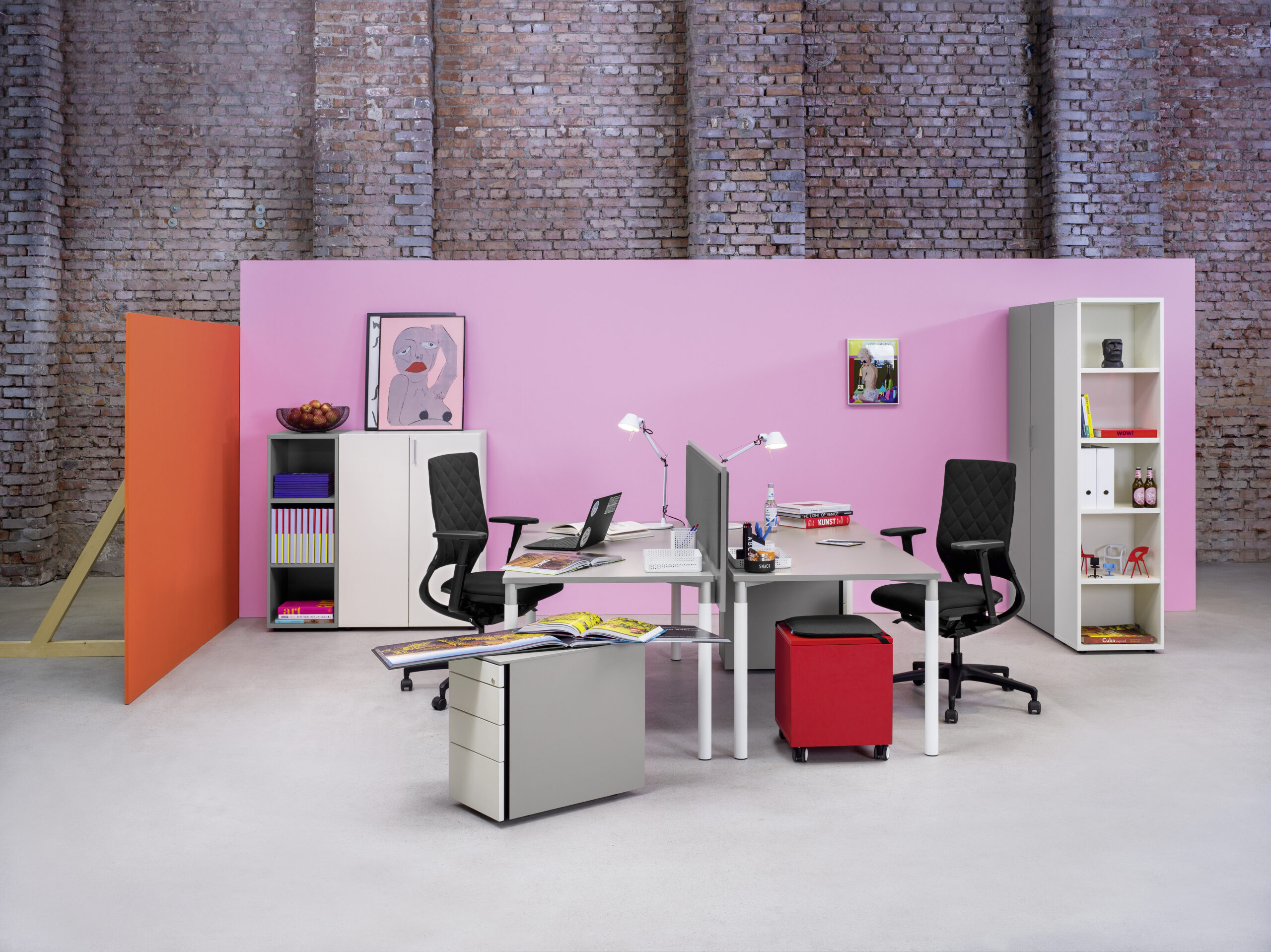 Homeoffice-Bereich mit Sitzhocker Bully, Schreibtisch und Skateboard vor blauer Wand