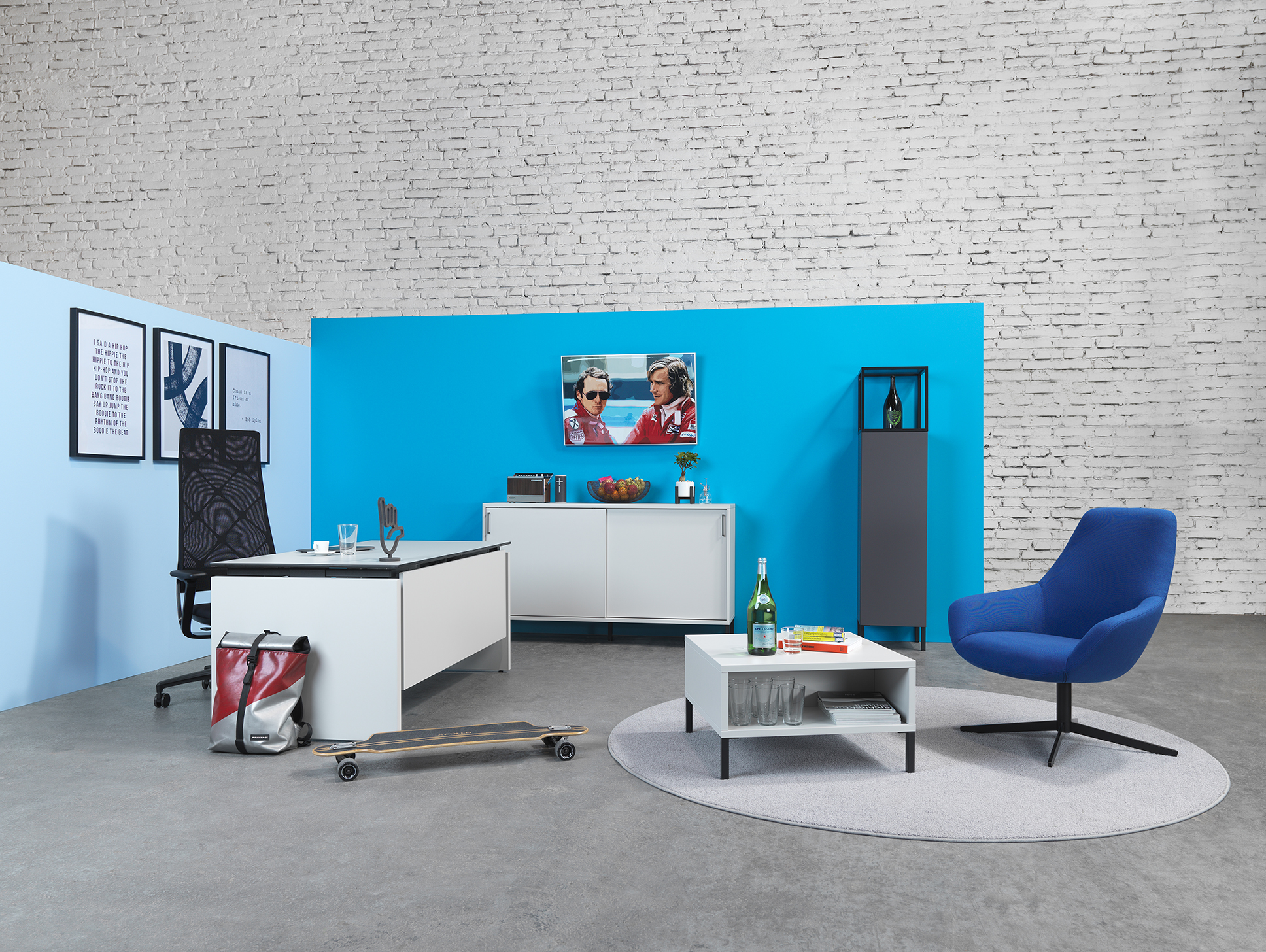 Homeoffice-Bereich mit Sitzhocker Bully, Schreibtisch und Skateboard vor blauer Wand
